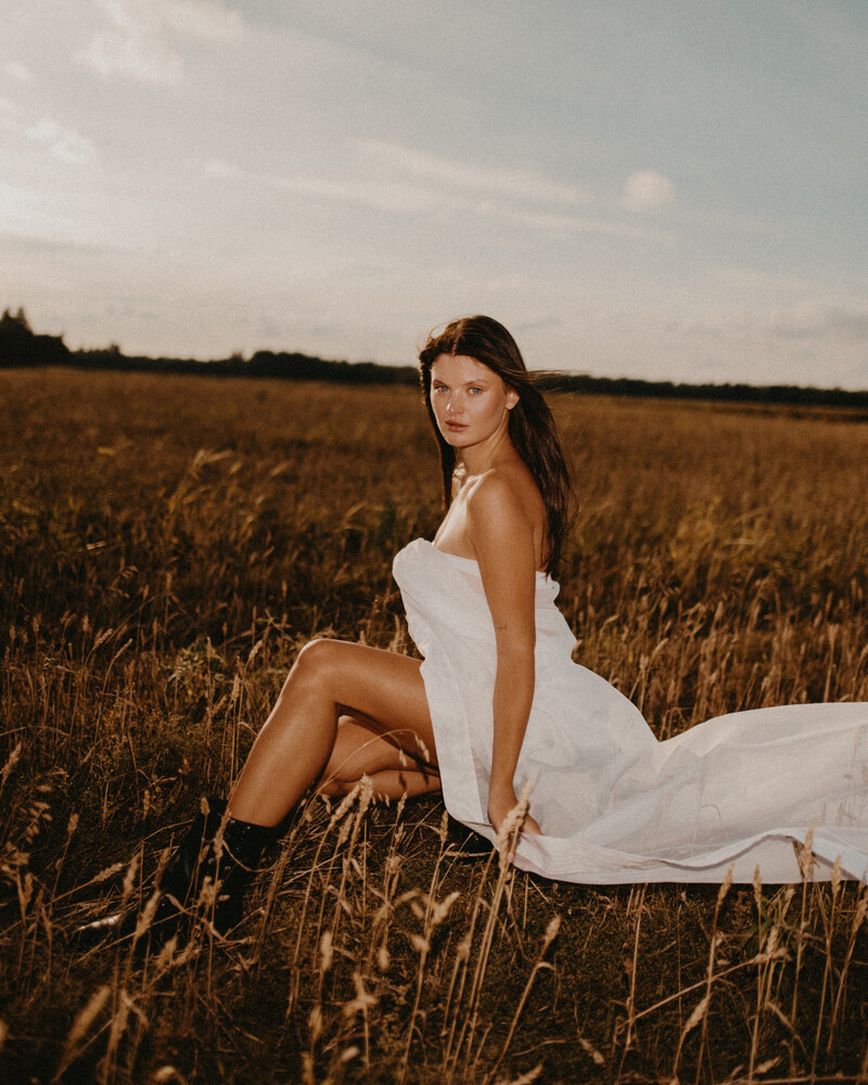 Woman in white dress seated in harvested grain field at golden hour