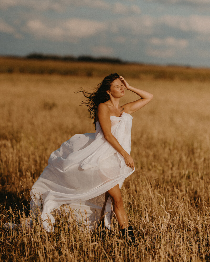 Woman in white dress posing in golden wheat field at golden hour