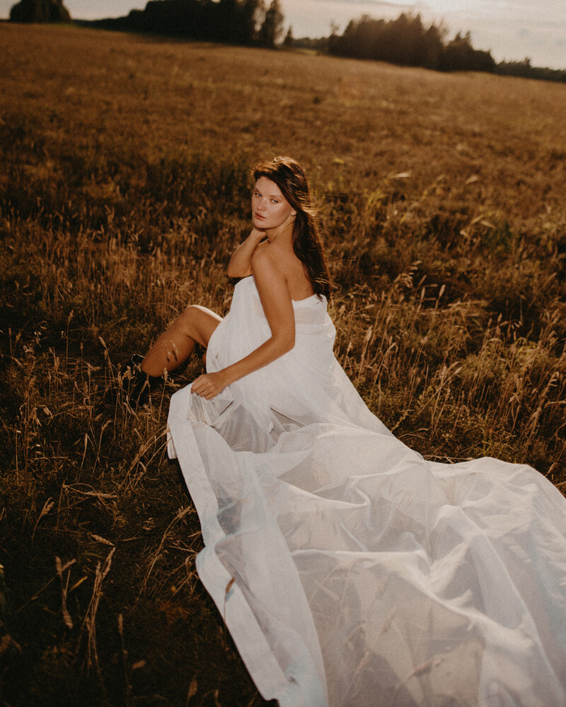 Woman in flowing white wedding dress standing in golden harvested field at sunset