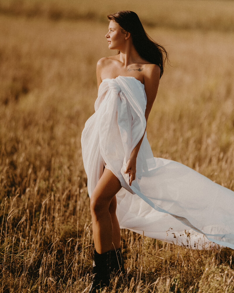 Woman in flowing white dress standing in golden dried grass field at golden hour