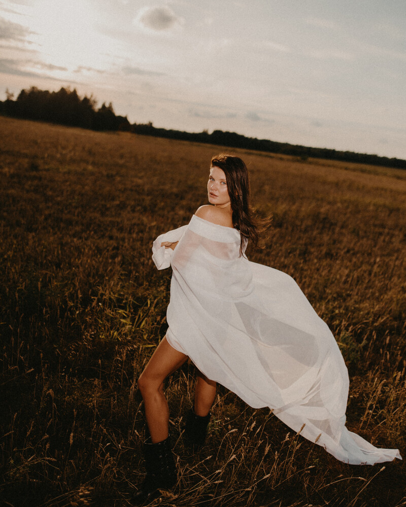 Woman in flowing white off-shoulder fabric posing in an open field during golden hour