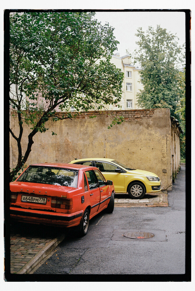 Two parked cars against a weathered tan building wall with trees overhead