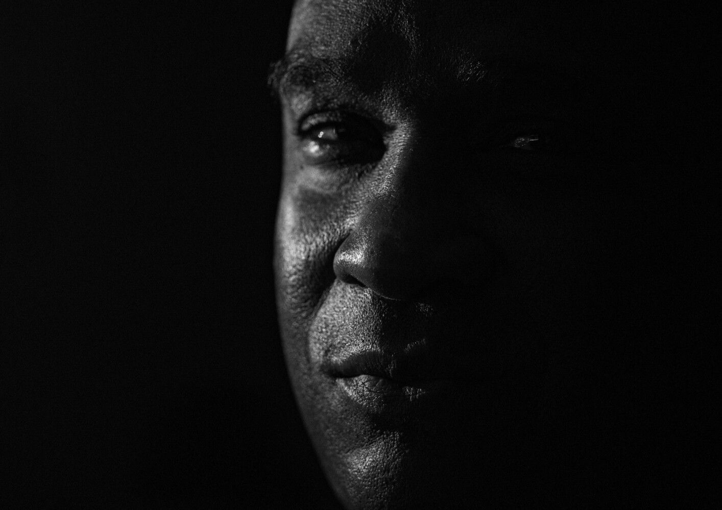 High-contrast black and white portrait of a man's face in profile against dark background