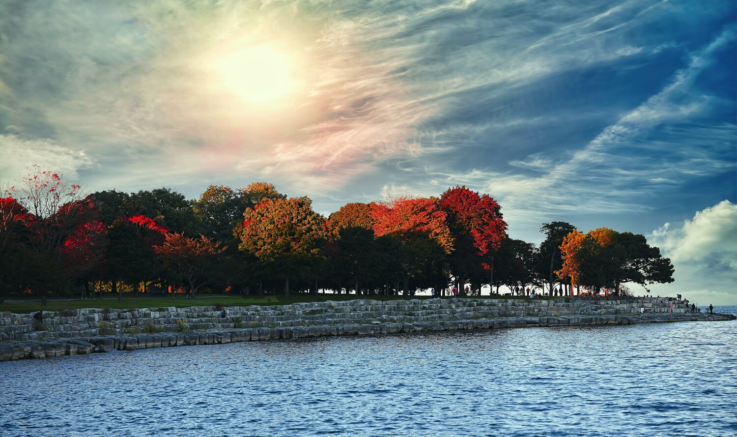 Waterfront landscape with autumn trees and stone seawall under dramatic sky