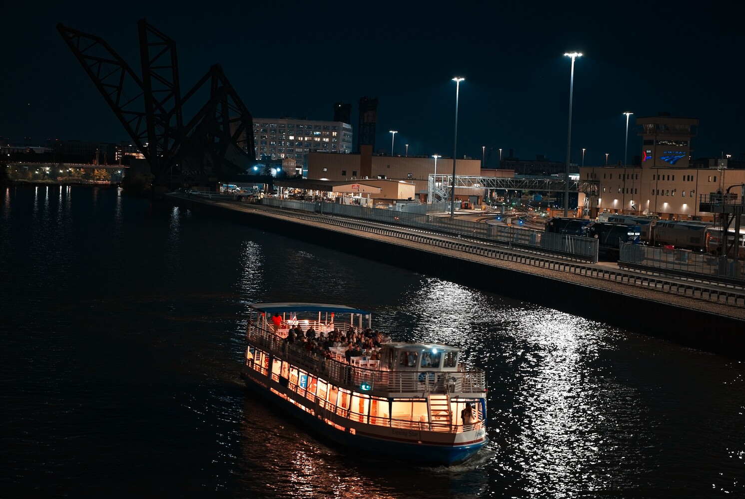 Illuminated tour boat on dark water at night with waterfront buildings and street lights in background