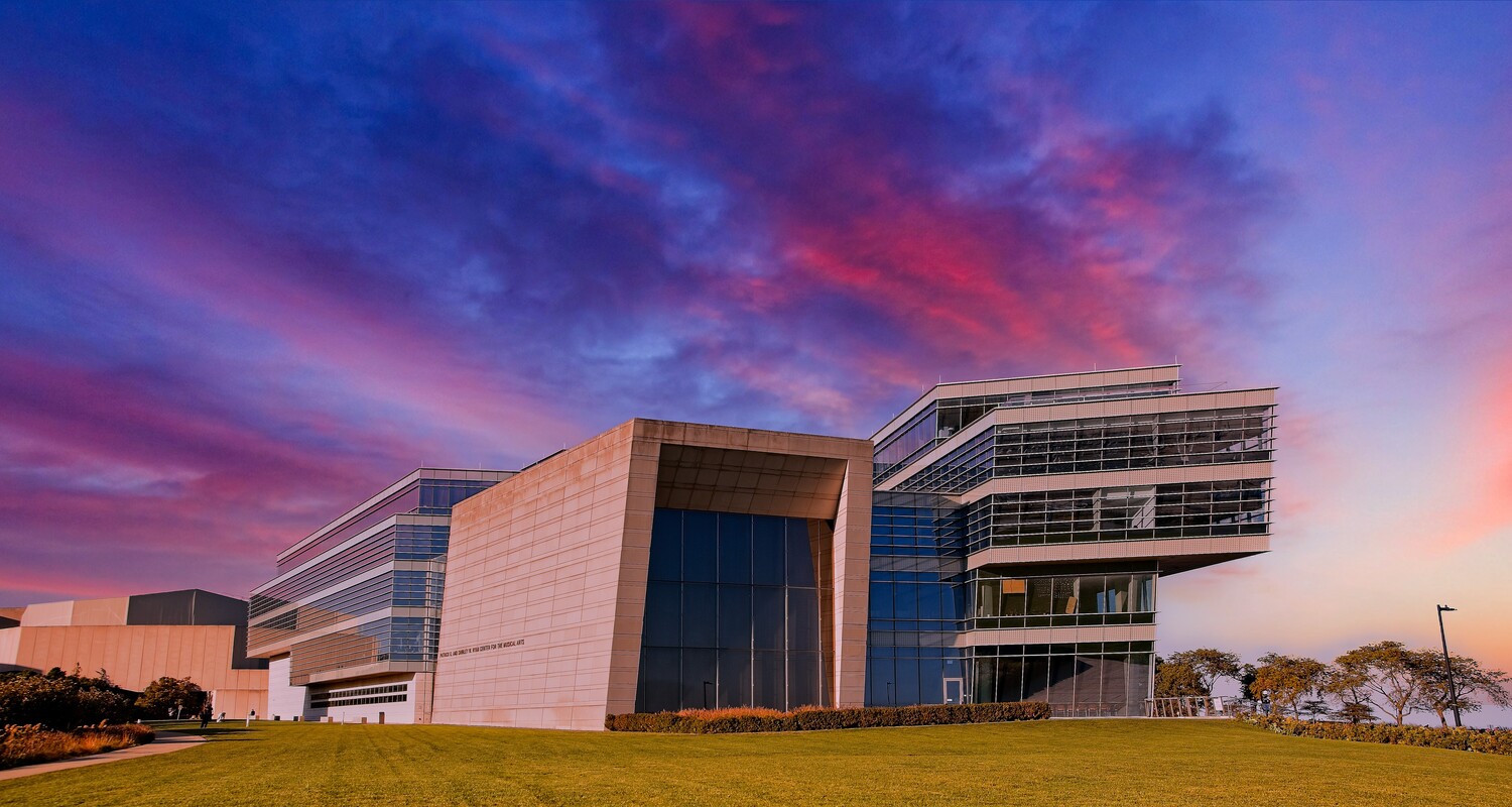 Modern curved architectural building with pink stone facade illuminated by vibrant purple and pink sunset sky