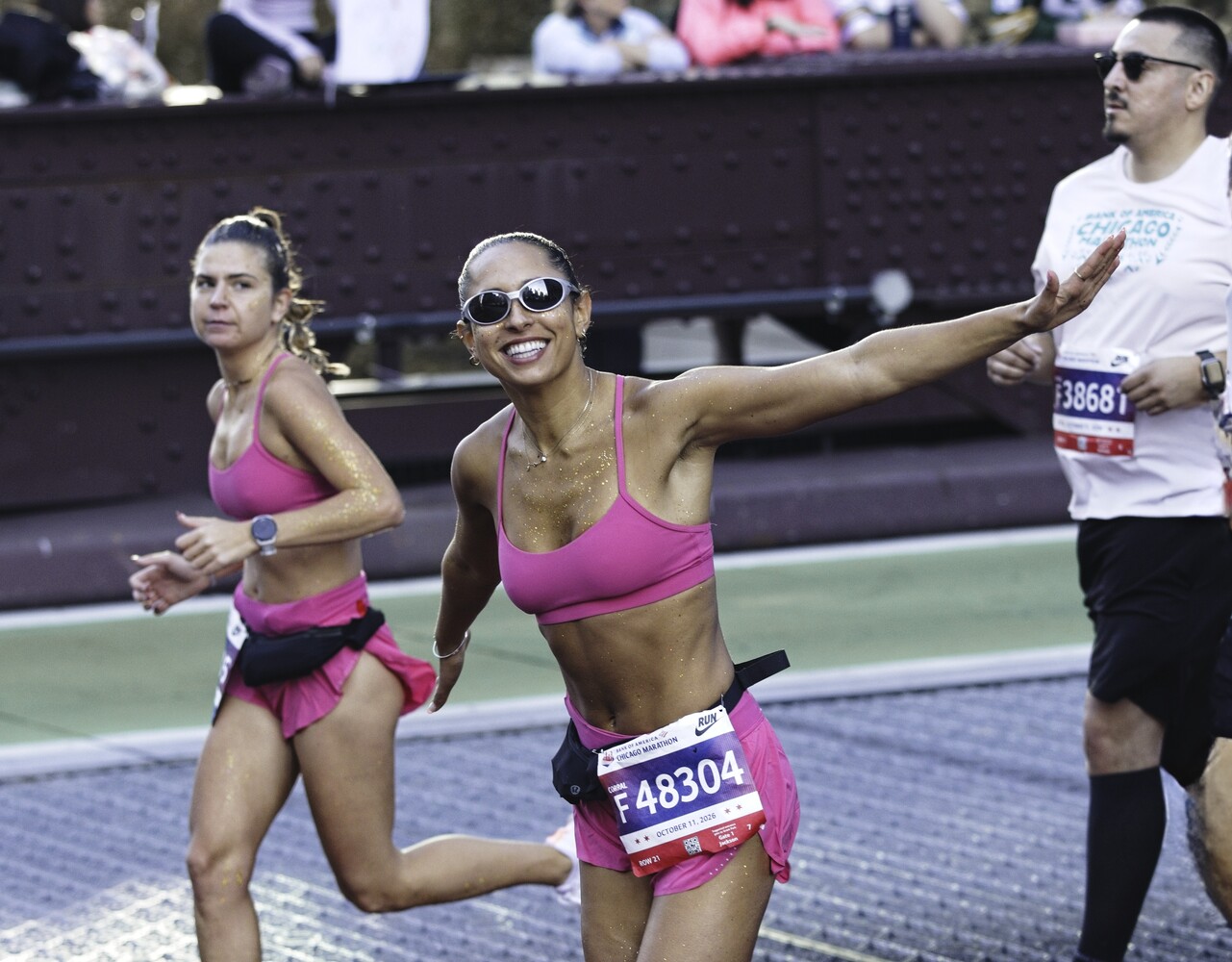 Female runners in pink athletic wear competing in a road race with spectators and officials visible