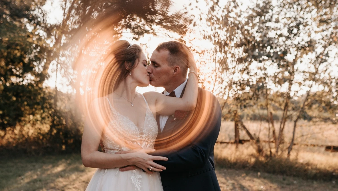 Bride and groom kissing outdoors with a glowing light streak effect around them.