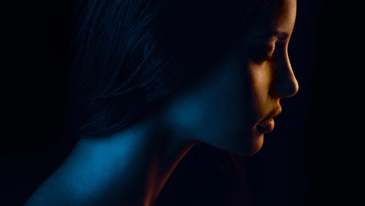 Profile of a person with warm and cool directional lighting creating dramatic contrast against a dark background.