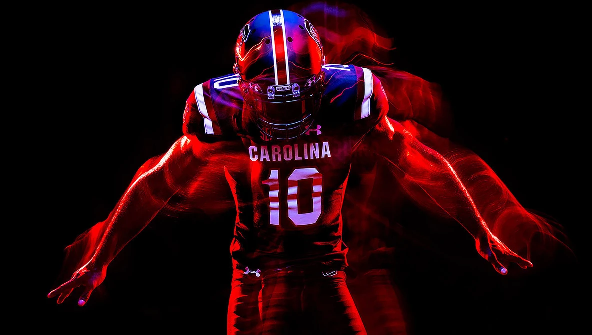 University of South Carolina football player wearing number 10 red jersey, photographed against black background with dramatic red and blue neon lighting effects.