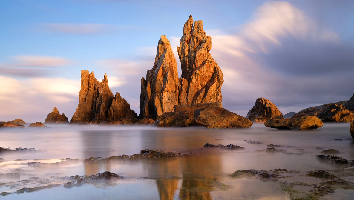 Dramatic rocky sea stacks rising from shallow water at golden hour with smooth water effect.
