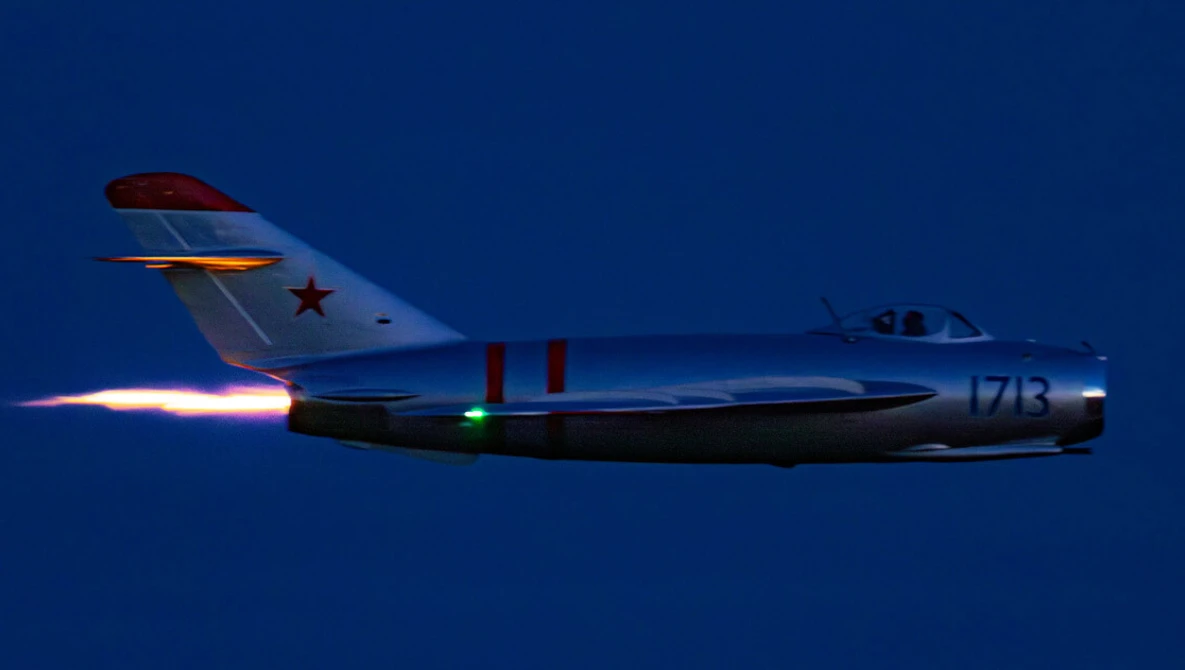 Soviet-era fighter jet in flight with afterburner engaged against deep blue sky