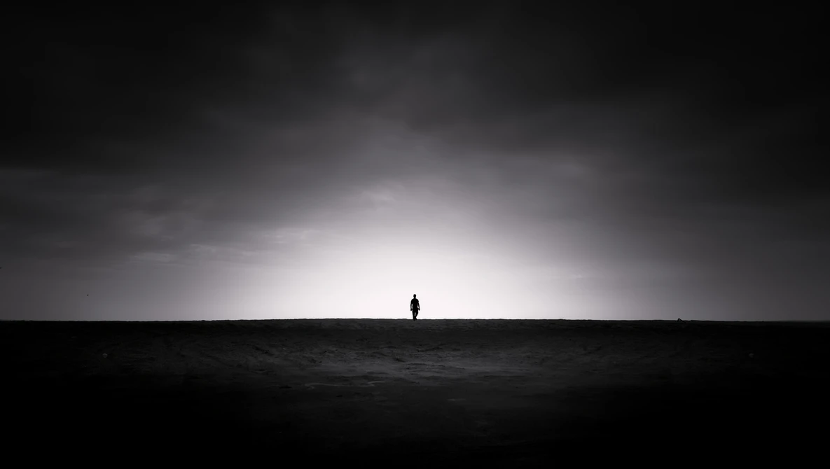 Silhouetted figure standing alone on a dark horizon beneath a dramatic cloudy sky with bright light breaking through.