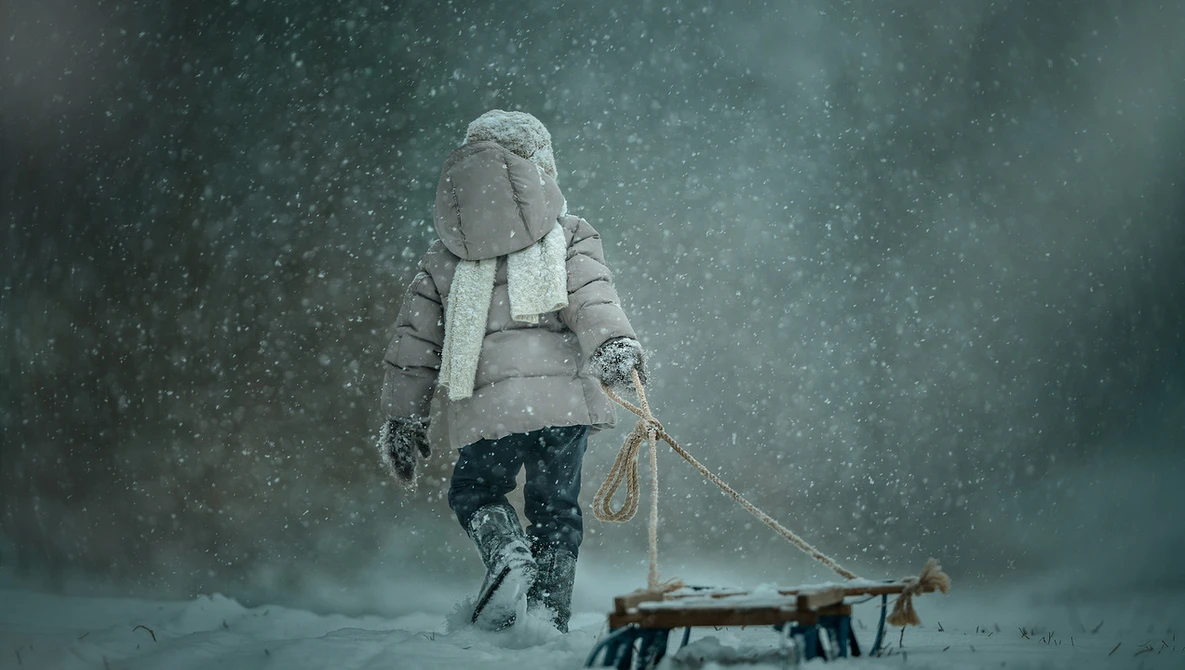 Person in winter clothing pulling a wooden sled through heavy snowfall.