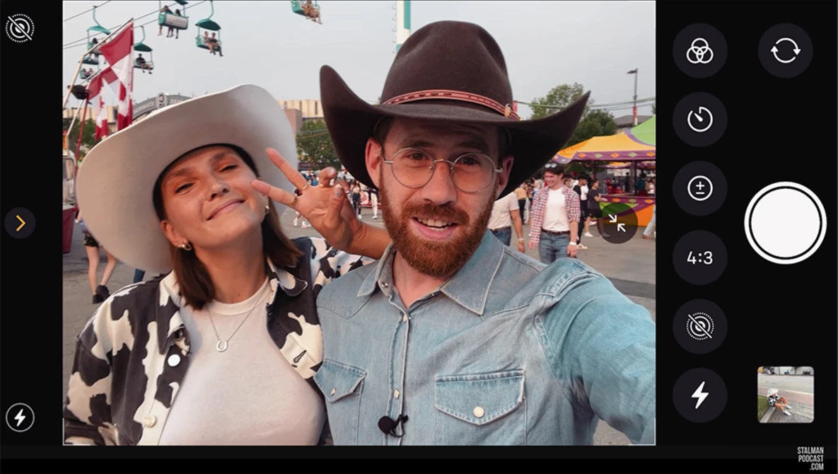 Two people in cowboy hats at a fairground during daytime, smiling at camera.