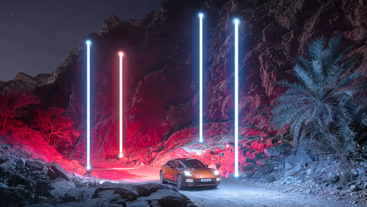 Sports car illuminated by vertical neon tubes in red and blue against rocky terrain at night.