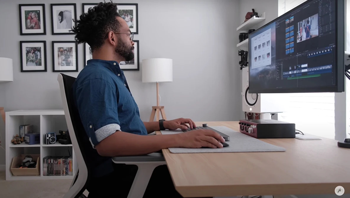 Video editor working at desktop with dual monitors displaying editing software interface.
