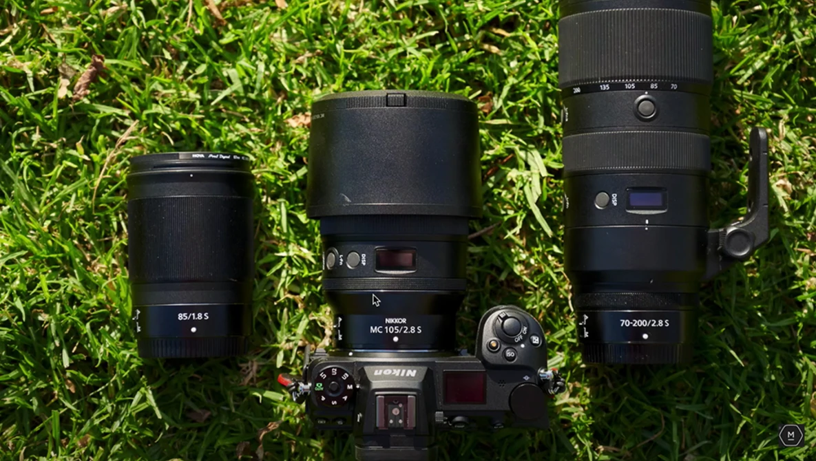 Camera body with three interchangeable lenses arranged on moss-covered ground.