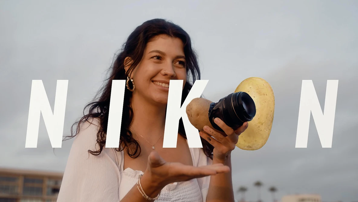 Female photographer holding a camera and gold reflector against sky backdrop.