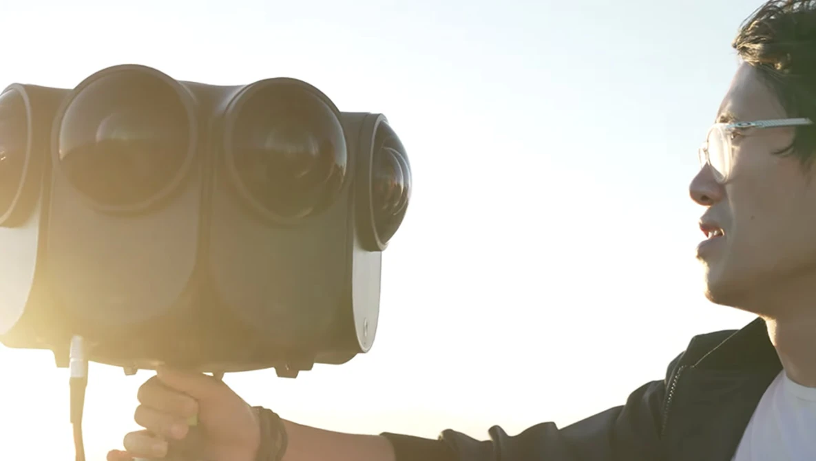 Photographer holding a professional cinema camera against bright sunlight, wearing sunglasses.