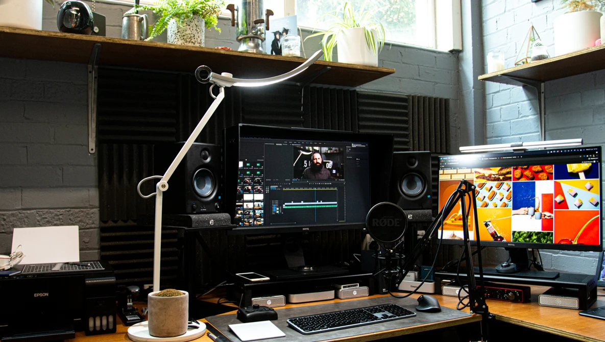 Professional video editing workspace with dual monitors, mixing console, studio speakers, and articulating desk lamp.