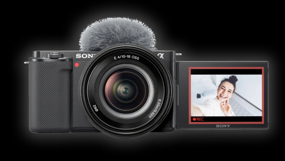 Sony mirrorless camera with attached microphone, flip-out LCD screen displaying video recording interface.