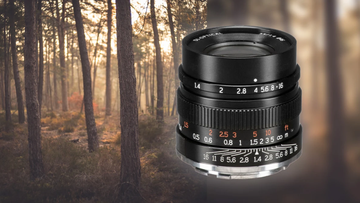 Black vintage rangefinder lens with aperture and focus markings displayed against a soft-focus autumn forest background.