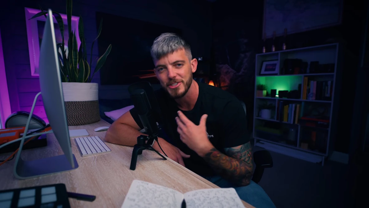 Content creator speaking into microphone at desk with studio lighting setup.