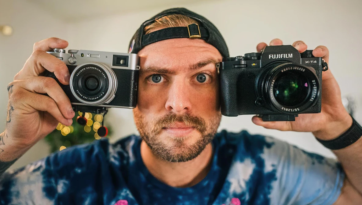 Photographer holding a rangefinder film camera and a Fujifilm mirrorless camera side by side.