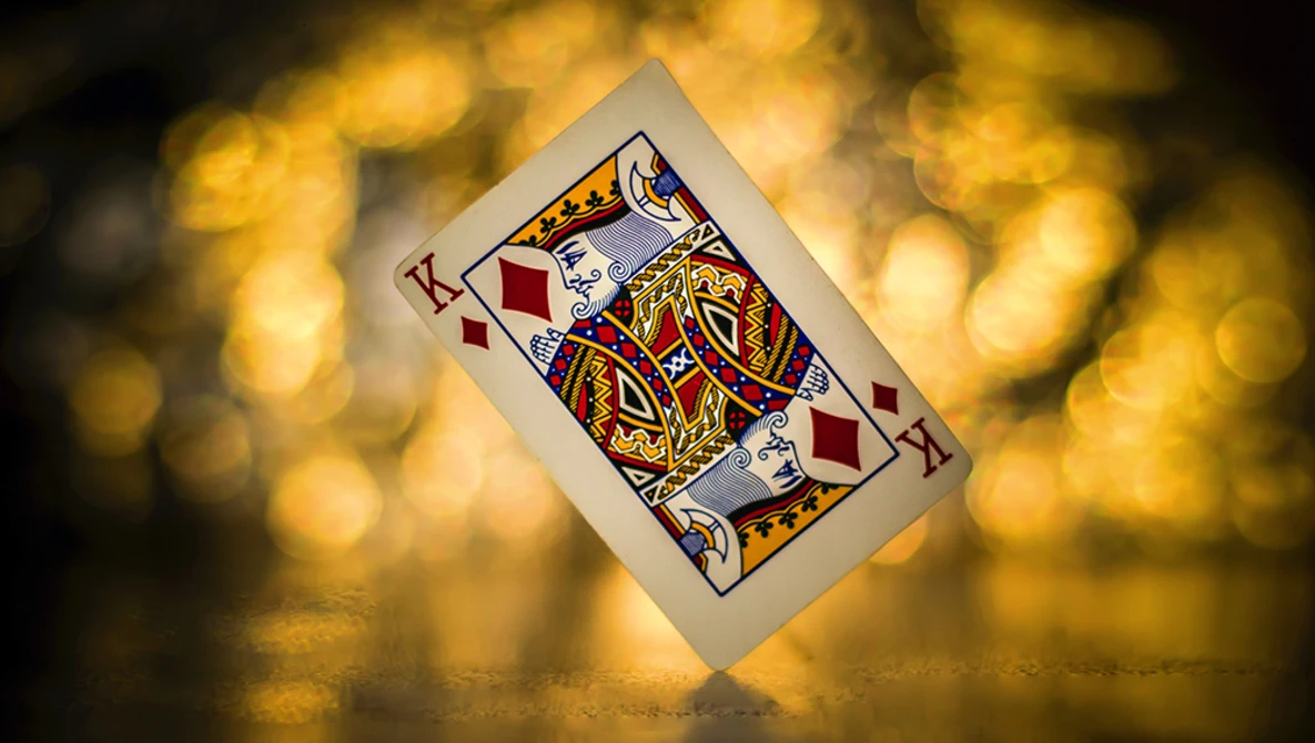 King of diamonds playing card tilted against golden bokeh background.