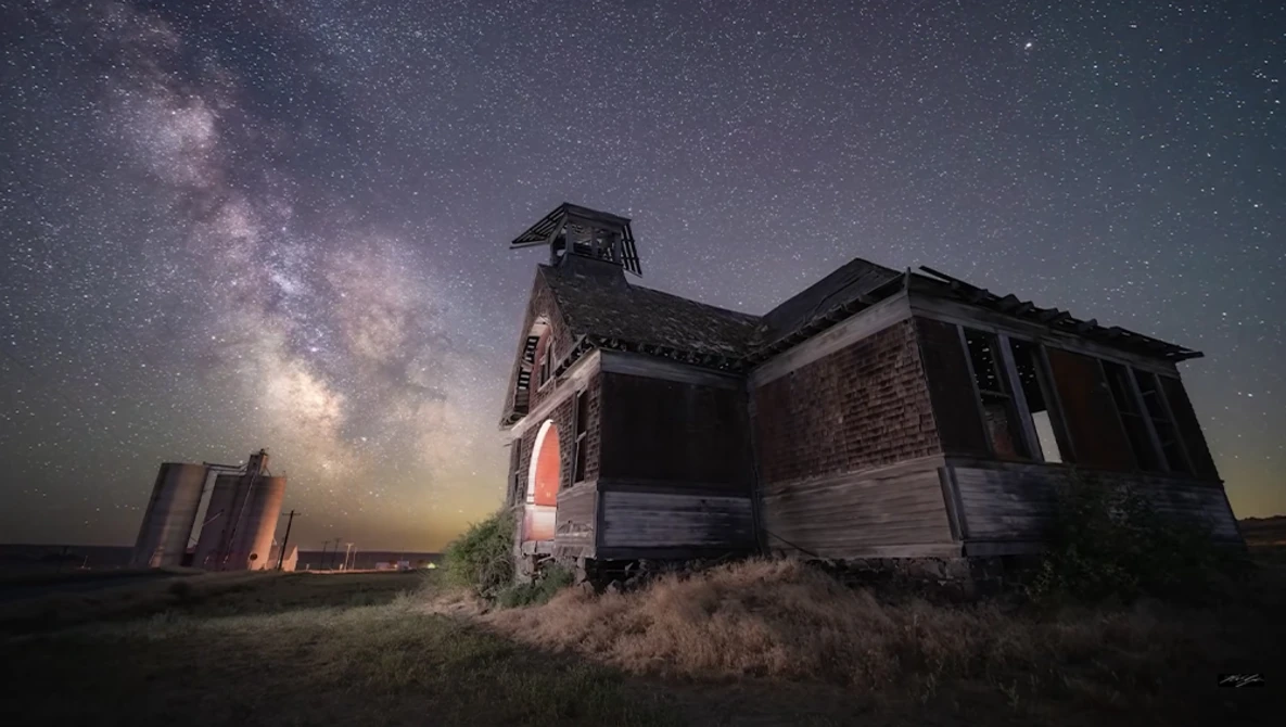 Abandoned brick schoolhouse silhouetted against the Milky Way galaxy at night.