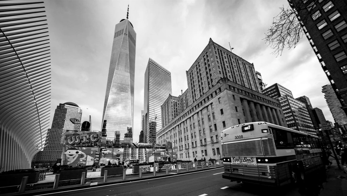 Black and white urban street scene featuring modern skyscrapers and a bus in a downtown area.