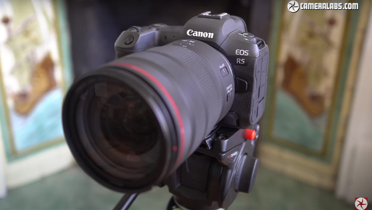 Canon EOS R5 mirrorless camera with a Canon RF telephoto lens mounted, displayed against a blurred interior background.