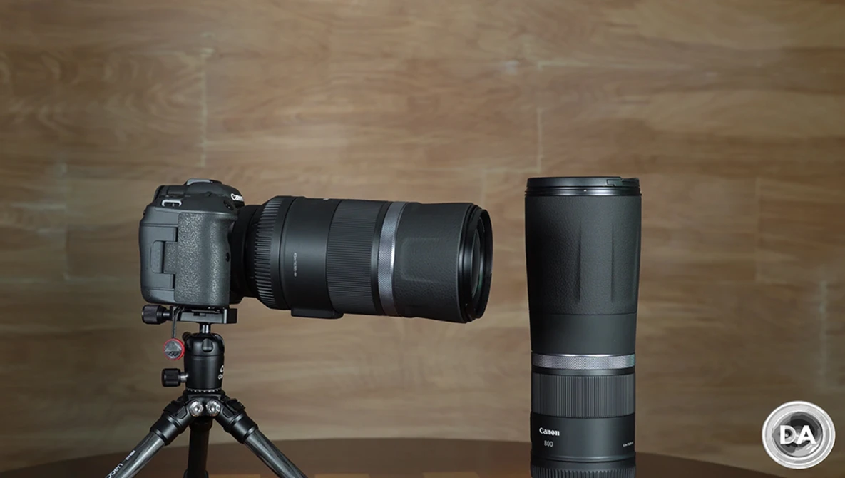 Canon telephoto lens mounted on DSLR camera on tripod, displayed alongside matching standalone lens on wooden background.