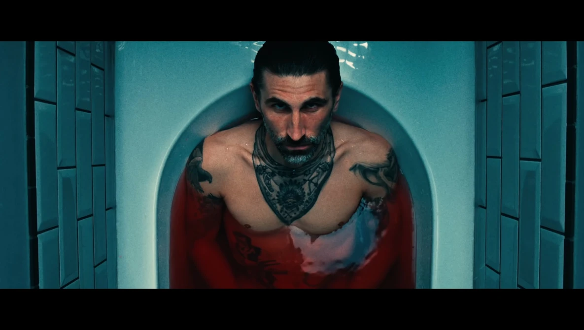 Shirtless man with tattoos and bandana in symmetrical pose under teal circular backdrop.