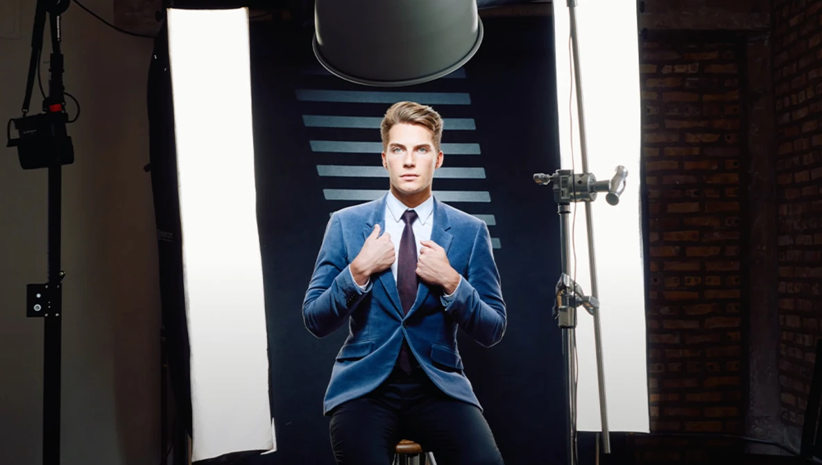 Professional headshot of a man in blue blazer and red tie against striped backdrop with studio lighting.