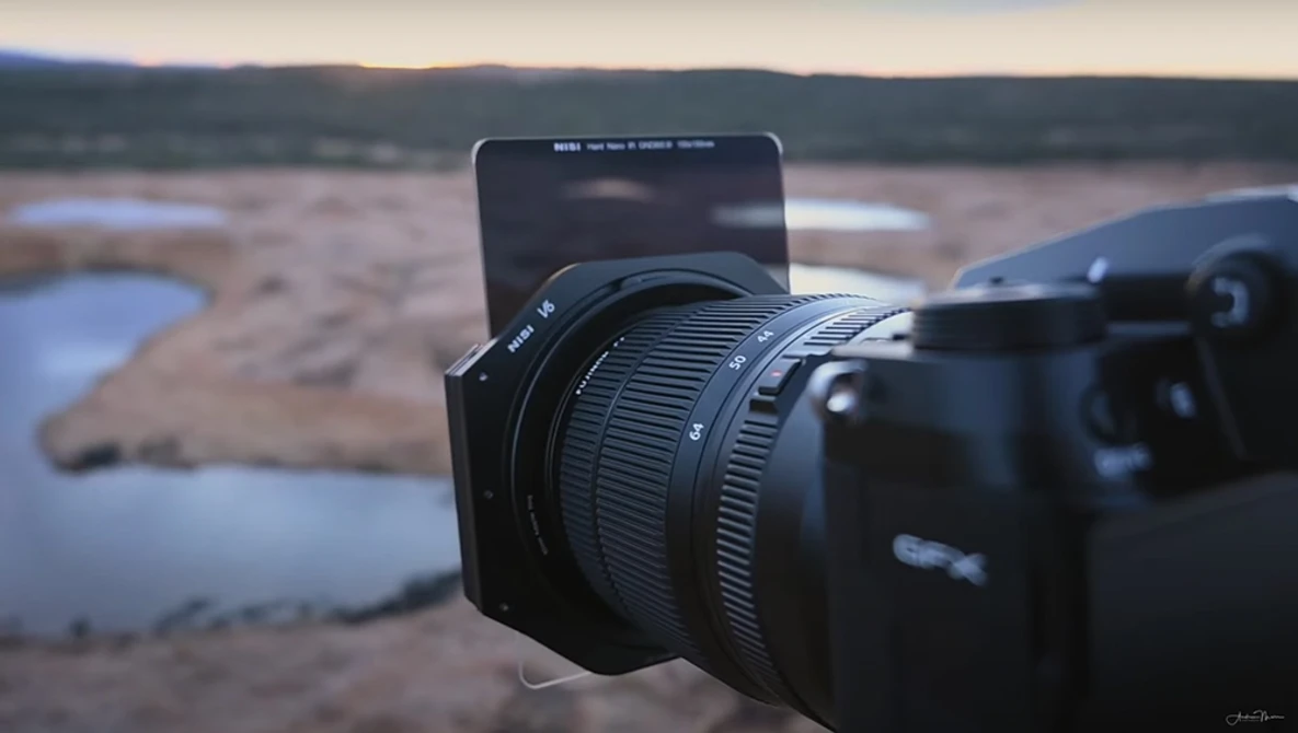 Camera with wide-angle lens mounted on tripod, pointing toward expansive landscape with distant water and hills.