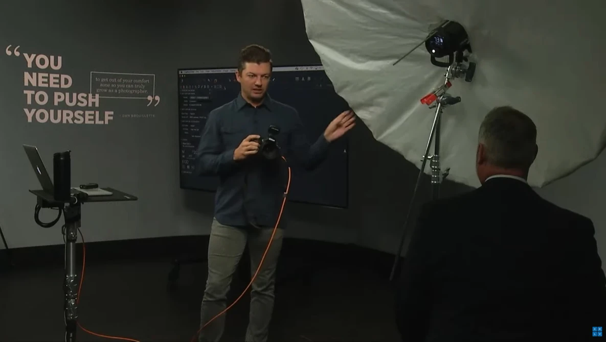Man speaking during photography workshop with studio lighting setup visible in background.
