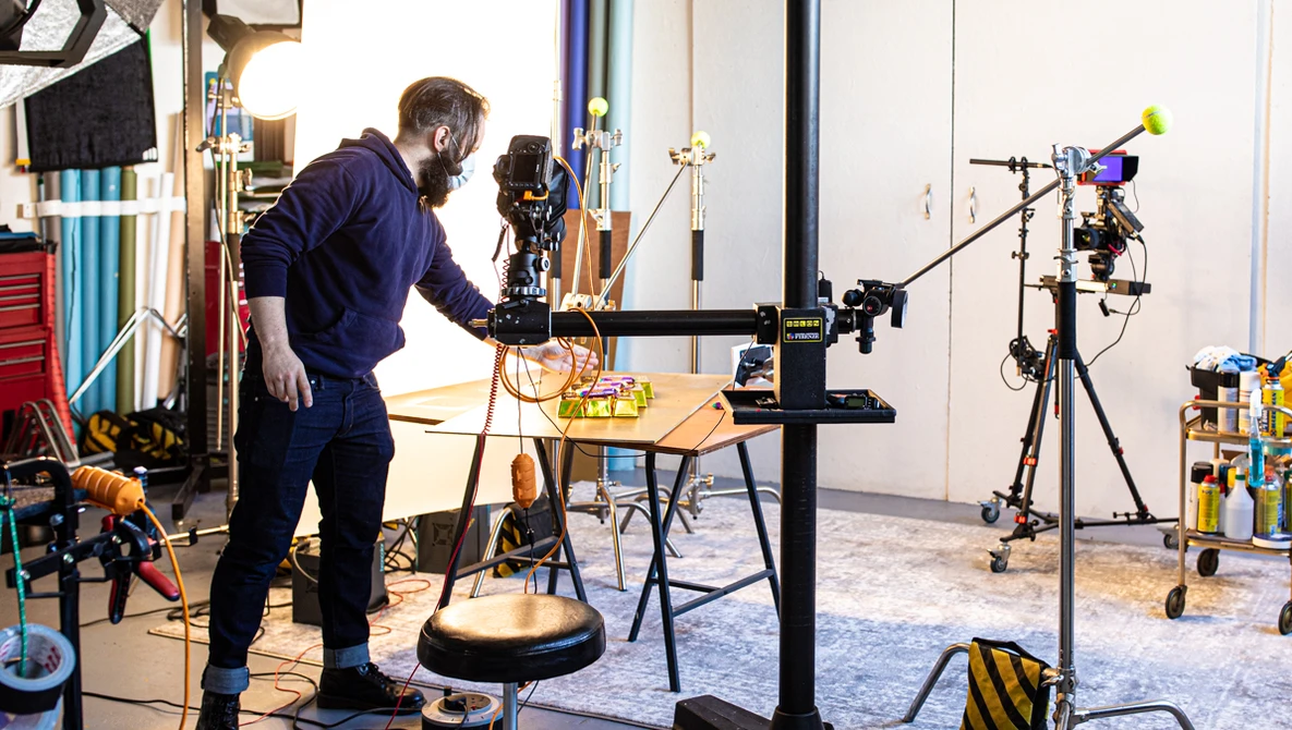 Photographer adjusting a camera on a tripod in a studio with multiple lighting rigs and equipment.