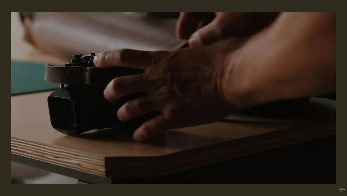Hands demonstrating operation of a compact camera on a wooden surface.
