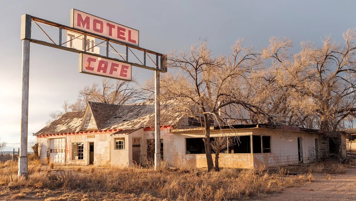 Abandoned motel and cafe with weathered wooden structures and vintage signage in desert landscape.