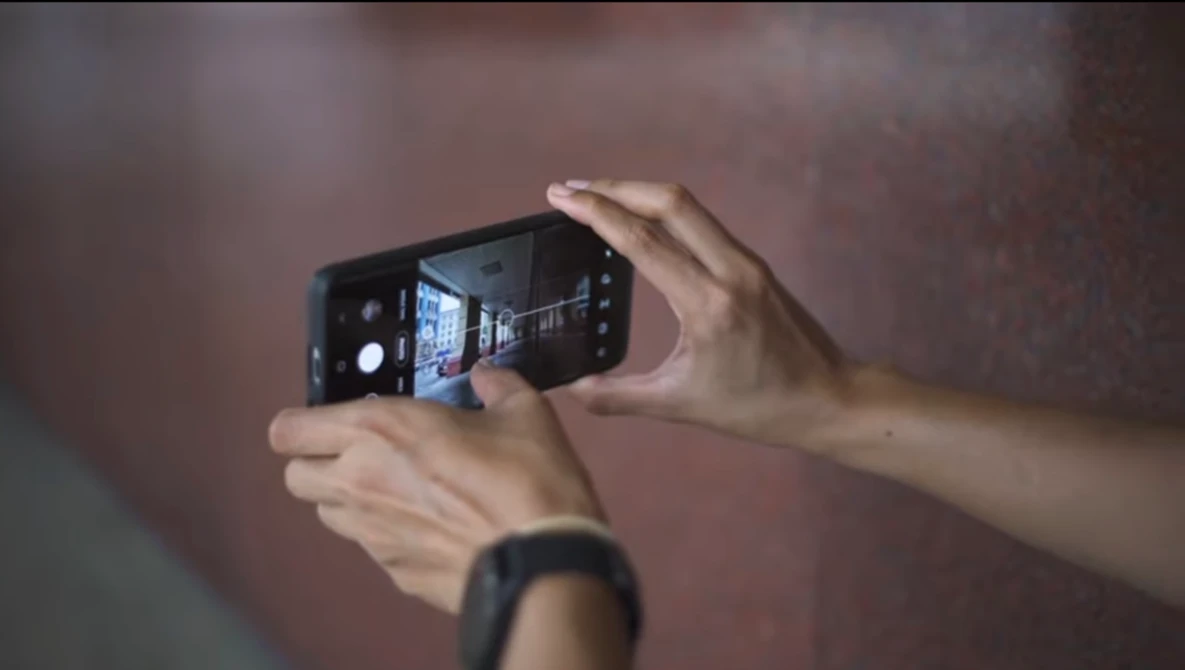 Hands holding a smartphone in landscape orientation while photographing an illuminated interior space.