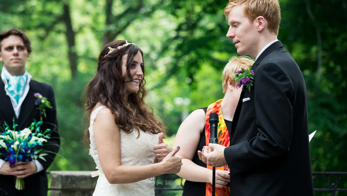 Bride and groom exchanging vows during outdoor wedding ceremony in natural green setting.