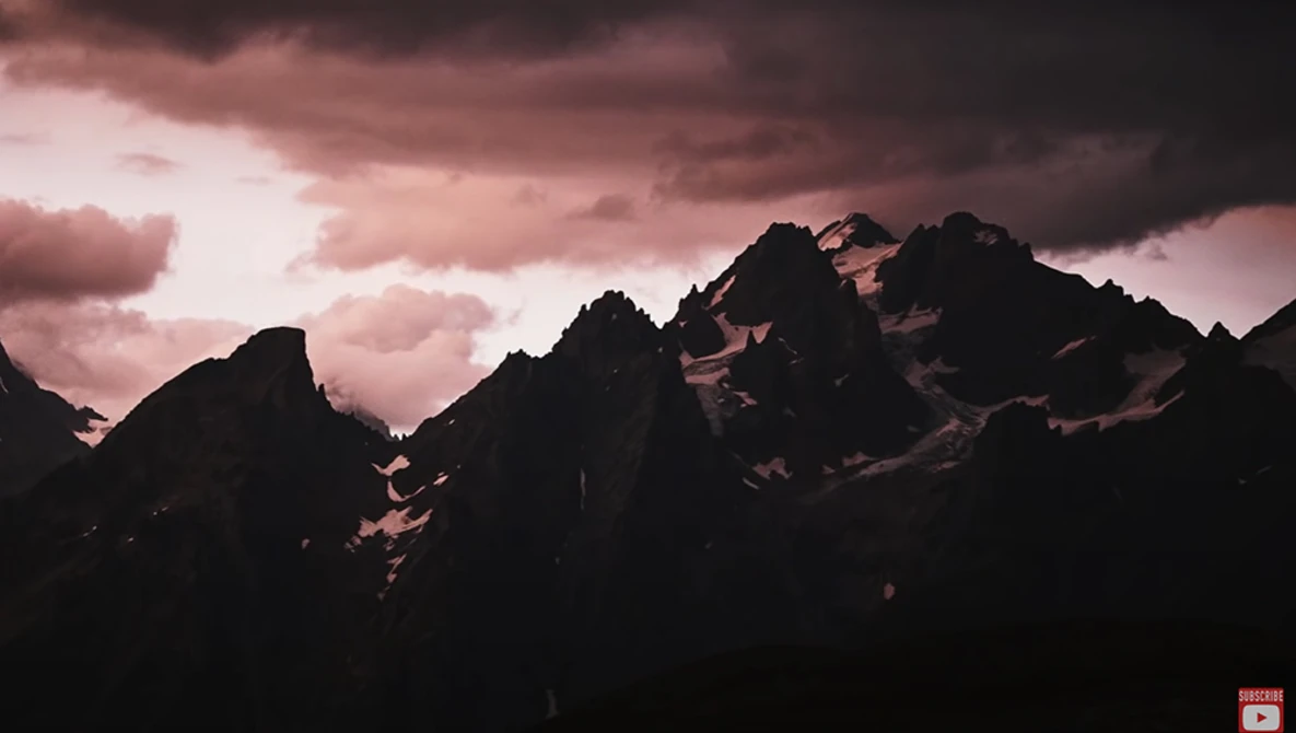 Jagged mountain peaks silhouetted against a dramatic pink and purple sky with storm clouds.
