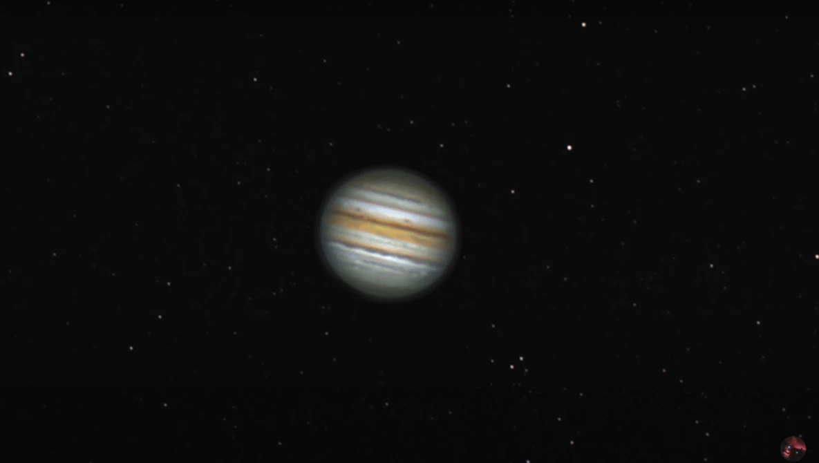 Jupiter captured through a telescope showing distinctive cloud bands and atmospheric detail against a starfield.