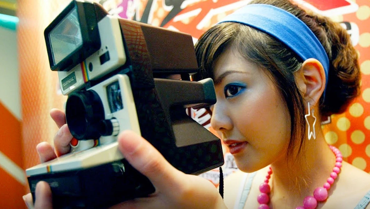 Photographer holding vintage instant film camera to her face against colorful patterned background.