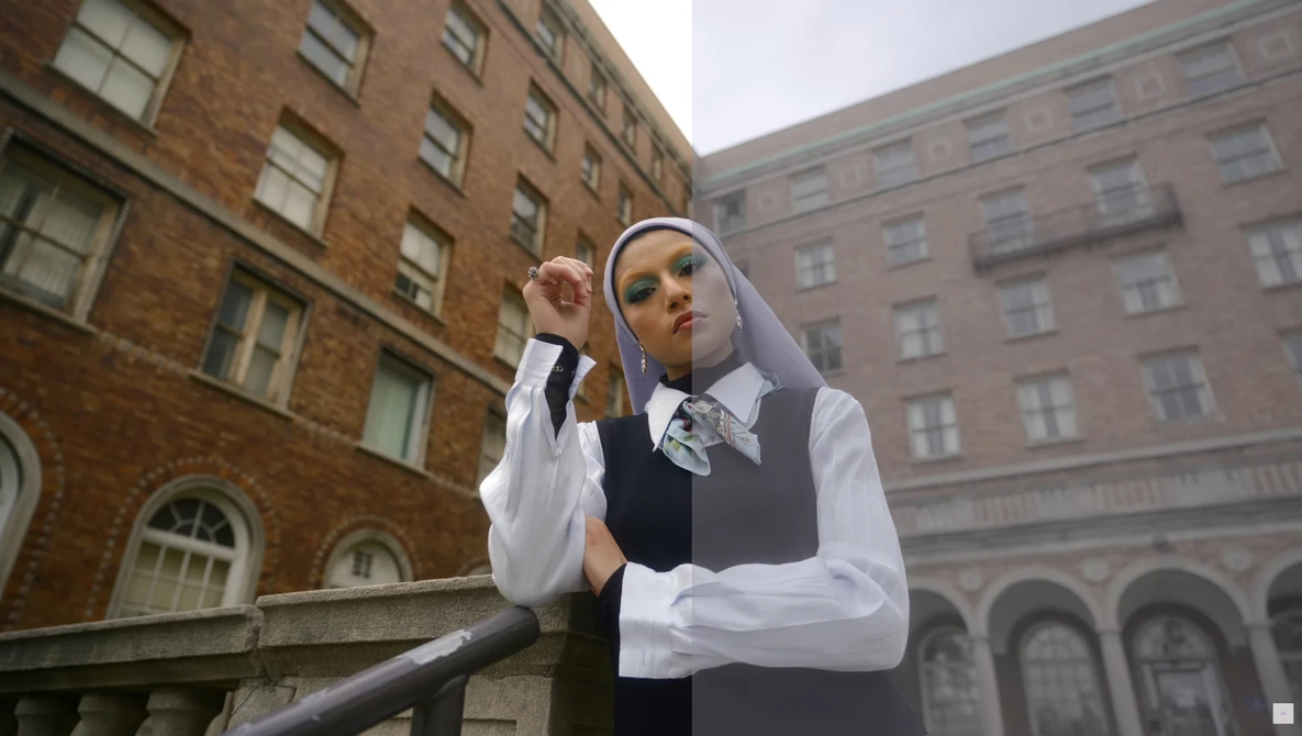Woman in nun habit and business vest adjusting her headpiece against urban brick buildings.