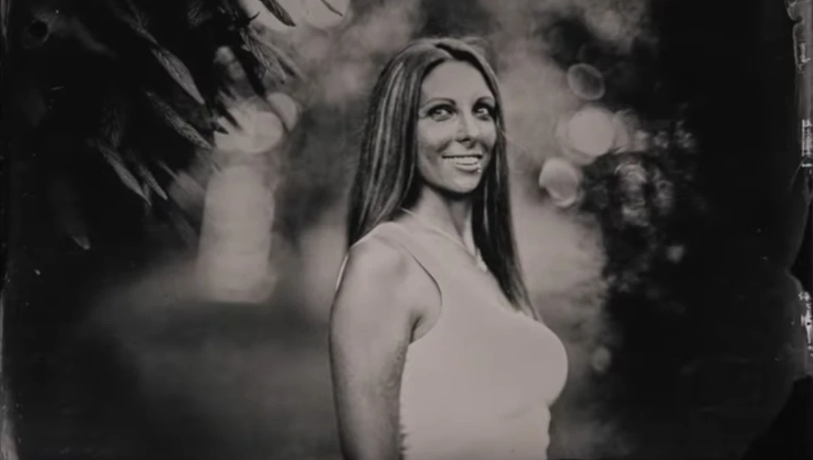 Woman in white tank top smiling over shoulder in black and white portrait.