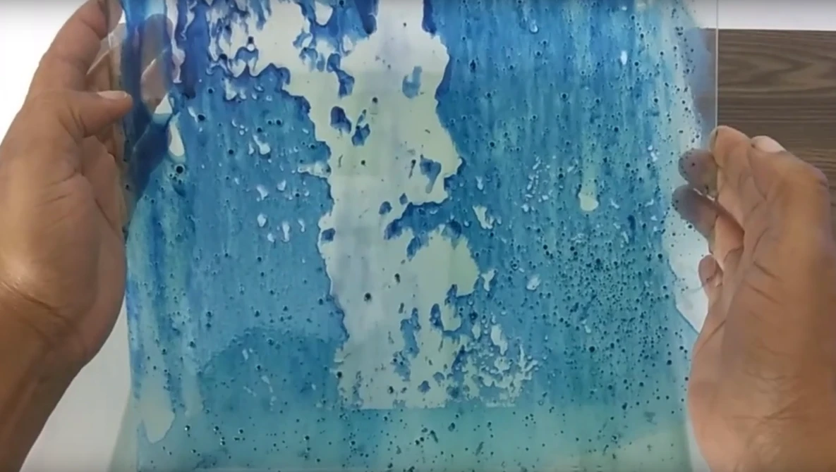 Hands holding a clear resin casting with blue and white swirled patterns and bubble textures.