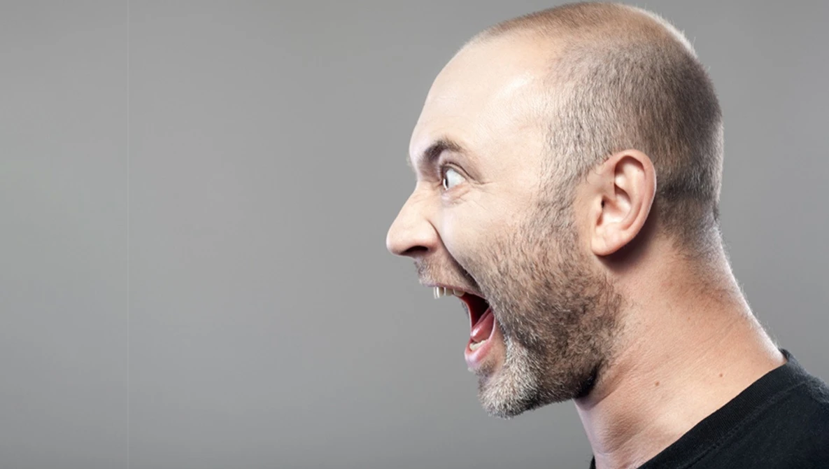 Man in profile with open mouth expressing surprise or excitement against neutral gray background.